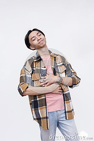 A blissful young asian man rubbing his stomach feeling satiated and full. Isolated on a white background Stock Photo