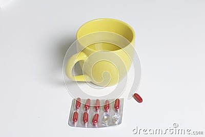 Blister with red pills. Several pills are missing. Nearby there is a mug with water and one pill for use. Stock Photo