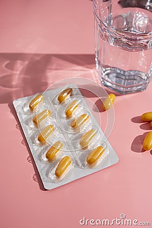 Blister with yellow pills, painkillers tablets with glass of water pink background, sun shadows Stock Photo