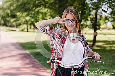 Blithesome girl in big headphones riding around park. Outdoor photo of laughing adorable lady sitti Stock Photo