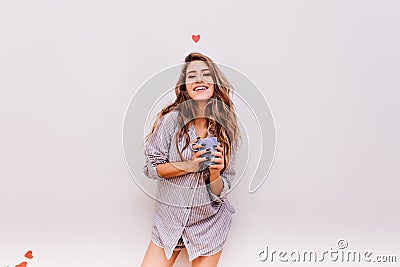Blithesome young woman in striped shirt laughing in morning in studio. Portrait of carefree white lady holding mug with Stock Photo