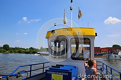 View on drivers cabin of small passenger and bicycle ferry voet- en fietsveer on river maas, container ship background in summer Editorial Stock Photo