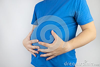 The man is holding onto his swollen belly. Bloating, flatulence, gas, malfunction of the gastrointestinal tract. Bending over in Stock Photo