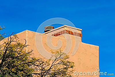 Block style chimney on an adobe house with tiny red tiles or bricks on vent with metal top and front or back yard tree Stock Photo