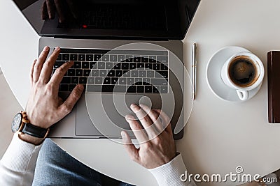 Blogger businessman guy in t-shirt working on a modern laptop in a bright office. Top view on white wooden desktop with laptop Stock Photo