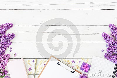 Blogger or freelancer workspace with clipboard, notebook, pen, lilac, box and petals on wooden background. Flat lay, top view. Bea Stock Photo