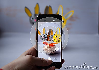 a blogger takes pictures of Easter bunnies made of c paper on his phone Stock Photo