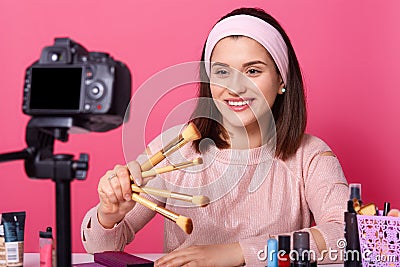 Blogging, modern technology and people concept. Happy smiling woman beauty video blogger holds brushes for makeup while recording Stock Photo