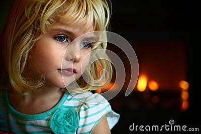 Blond blue eyed little girl sitting in front of a fireplace Stock Photo