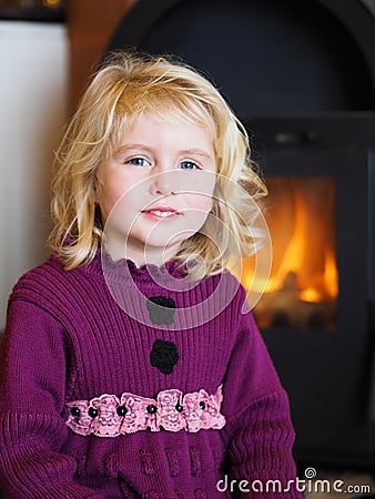 Blond blue eyed little girl sitting in front of a fireplace Stock Photo