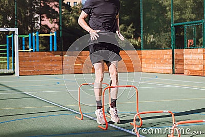 Blond boy in sportswear jumps over red obstacles to improve lower body dynamics. Plyometric training in an outdoor environment. Stock Photo