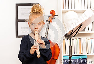 Blond curly girl plays flute standing near cello Stock Photo