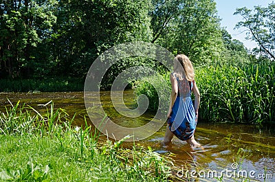 Blond girl blue mottled dress wade flowing river Stock Photo