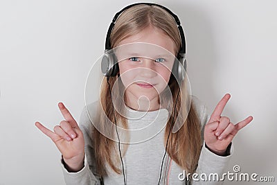 Blond girl with headphones listening music and singing. Cute little girl making a rock-n-roll sign. Stock Photo