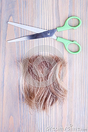 Blond hair lock, metal open scissors light wooden background close up, cut off natural blonde hair curl on bright wood, shears Stock Photo