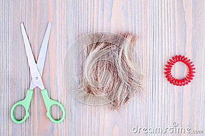 Blond hair lock, scissors, scrunchie light wooden background close up, cut off blonde hair curl on bright wood, shears, hair band Stock Photo
