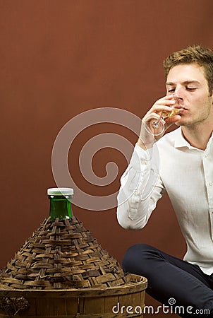 Blond handsome man drinking a glass of white wine near a carboy Stock Photo