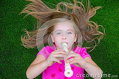 Blond kid children girl playing flute lying on grass Stock Photo