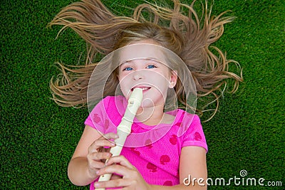 Blond kid children girl playing flute lying on grass Stock Photo