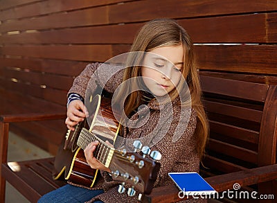 Blond kid girl learning play guitar with smartphone Stock Photo