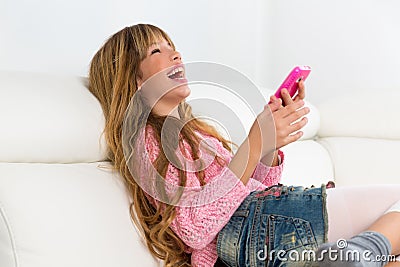 Blond kid girl playing fun with mobile phone on white sofa Stock Photo