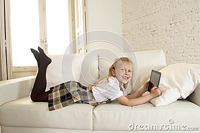Blond little girl lying on home sofa couch using internet app on digital tablet pad on digital tablet pad Stock Photo