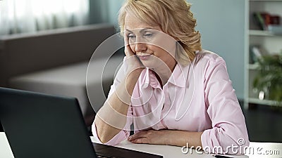 Blond middle-aged woman feeling bored watching online video, falling asleep Stock Photo