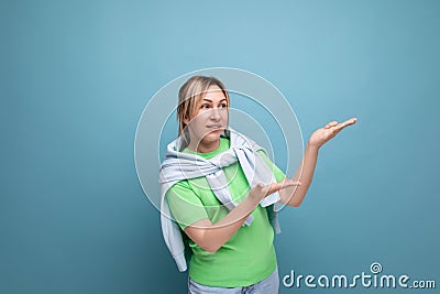 blond positive bright girl in a casual outfit shows her hand at a banner on a blue background with copy space Stock Photo