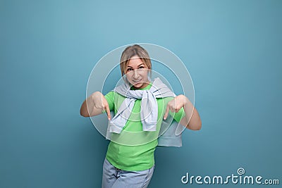 blond positive bright girl in a casual outfit shows her hand at a banner on a blue background with copy space Stock Photo