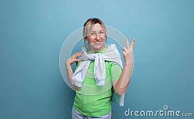 blond positive bright girl in a casual outfit shows two fingers on a blue background with copy space Stock Photo