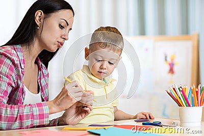 Blond smiling little boy hold in hand pencil drawing something together with mom. Stock Photo