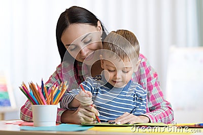 Blond smiling little boy hold in hand pencil drawing something together with mom. Stock Photo