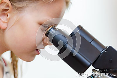 A blond 7 year old schoolchild looks into the eyepiece of a microscope. Isolated Stock Photo