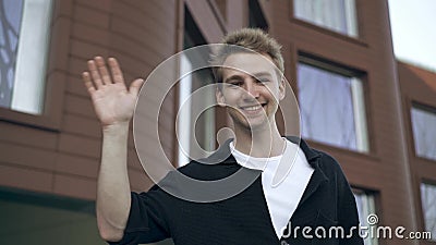 Blond young man waving hand standing near his house stock video footage Blond young man waving hand standing near his house stock video footage