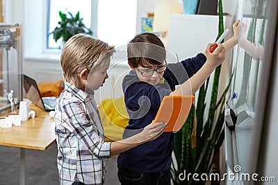 Blonde boy carrying orange tablet while his friend writing on the desk Stock Photo