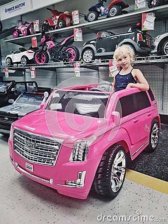 Blonde Caucasian girl sitting posing in large huge pink Cadillac car in kids children store Toys Are Us. Editorial Stock Photo