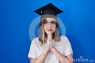 Blonde caucasian woman wearing graduation cap praying with hands together asking for forgiveness smiling confident Stock Photo