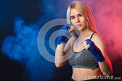 Blonde female athlete is exercising in defense on dark smoky background. Stock Photo