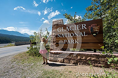 Blonde female stands and poses next to the Glacier National Park Sign in Montana USA Editorial Stock Photo