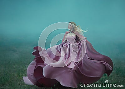 Blonde in the fog in a light long expensive royal dress fluttering on the fly, takes the form of a magic flower, a Stock Photo