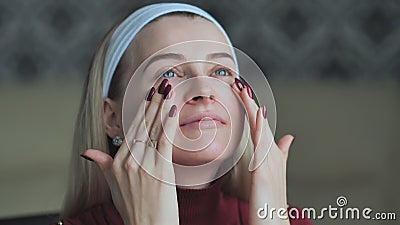 Blonde girl applies concealer on face before make-up. Stock Photo