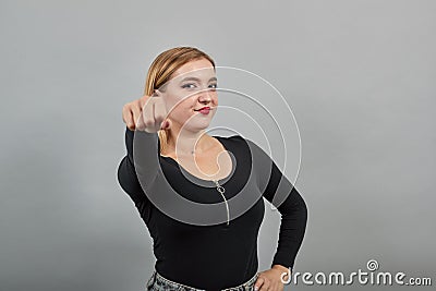 Blonde girl in black jacket on grey background: woman shows off fist, smiles Stock Photo