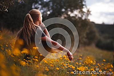 Blonde girl sitting in a field of yellow flowers Stock Photo