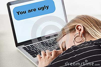 Blonde girl sleeping near laptop with you are ugly message on screen, cyberbullying concept. Stock Photo