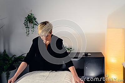 blonde haired woman beautician, concentrated and professional, preparing the massage table to start the day. Stock Photo
