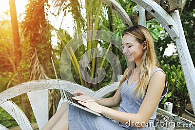 Blonde happy woman uses laptop for work on sunny day, background of sunshine green palms in Thailand, Phuket travel Stock Photo