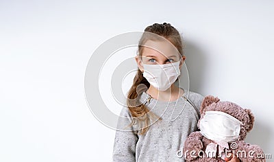 Little model in gray jumper and medical mask, posing isolated on white. Holding toy teddy bear which is also in mask Stock Photo