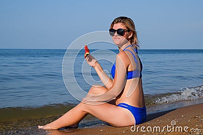 A blonde in sunglasses eats a watermelon by the sea. A juicy watermelon in the hands of a woman Stock Photo