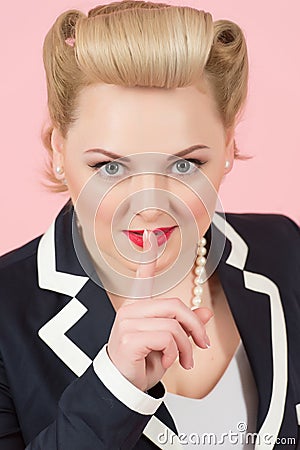 A blonde curl woman portrait with beautiful make-up with finger over lips. Girl keeps silent looking into camera. Close up of face Stock Photo