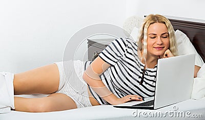 Blonde woman reading blogs on laptop in bed Stock Photo